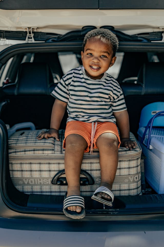 kleiner Junge sitzt auf einem Koffer hinten im Auto